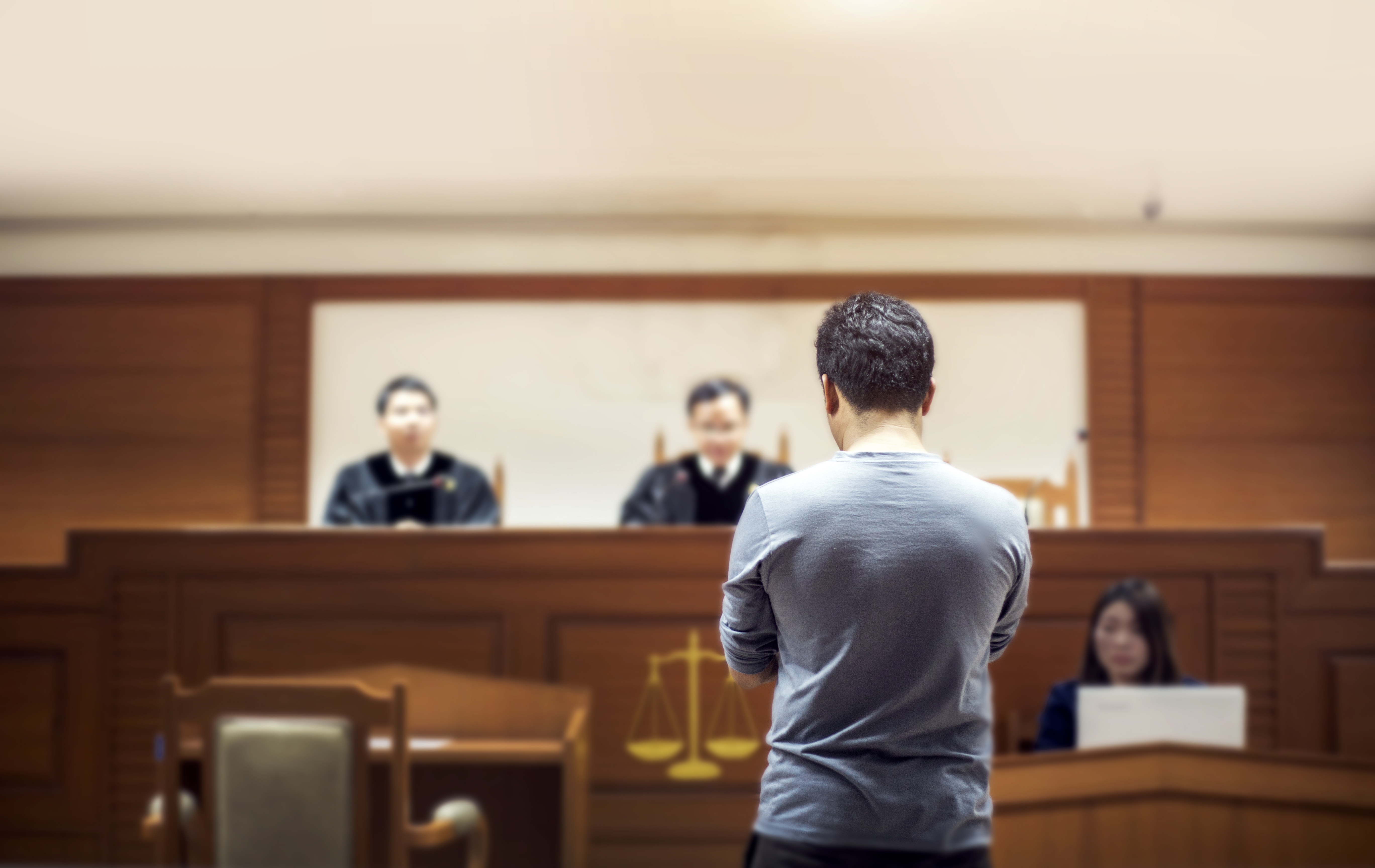 A man standing in court before judges, attending a legal hearing to apply for estate administrator appointment.