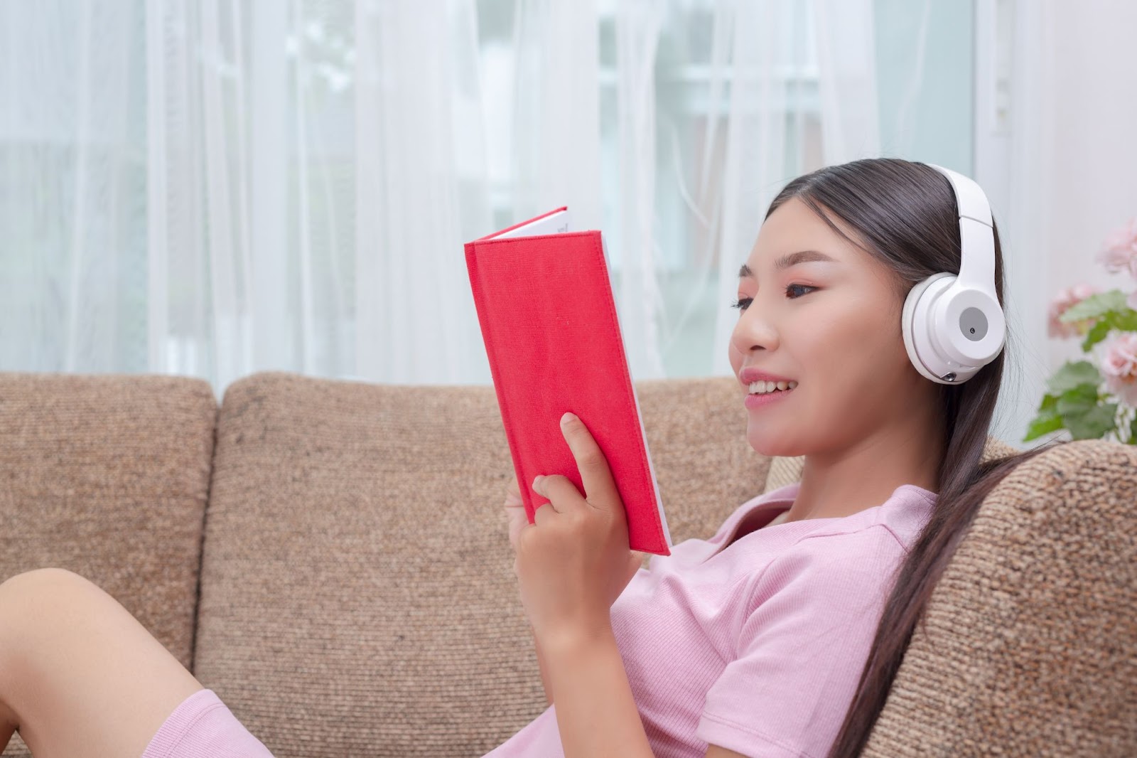 A girl listening and reading a book on sofa.